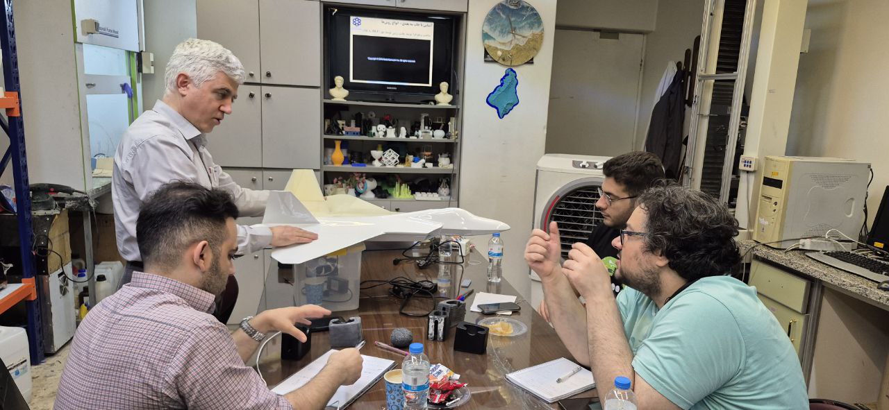 تیم مهندسی در یک جلسه فنی، در حال بررسی یک ماکت بزرگ هواپیمای جنگنده که با استفاده از تکنولوژی پرینت سه بعدی ساخته شده است.